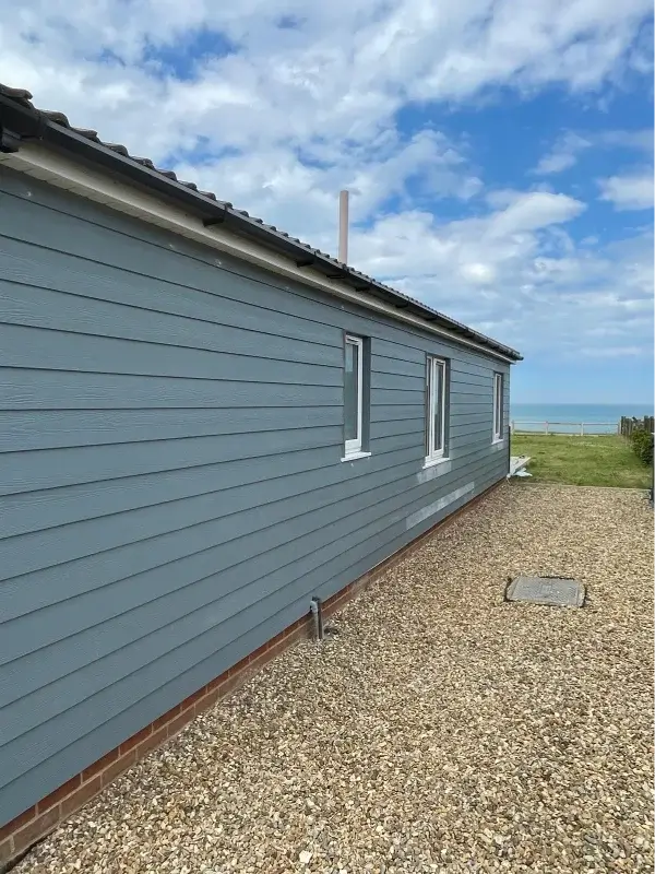 Blue-grey horizontal cladding installed along a coastal bungalow with white-framed windows. By Norfolk Exterior Solutions.